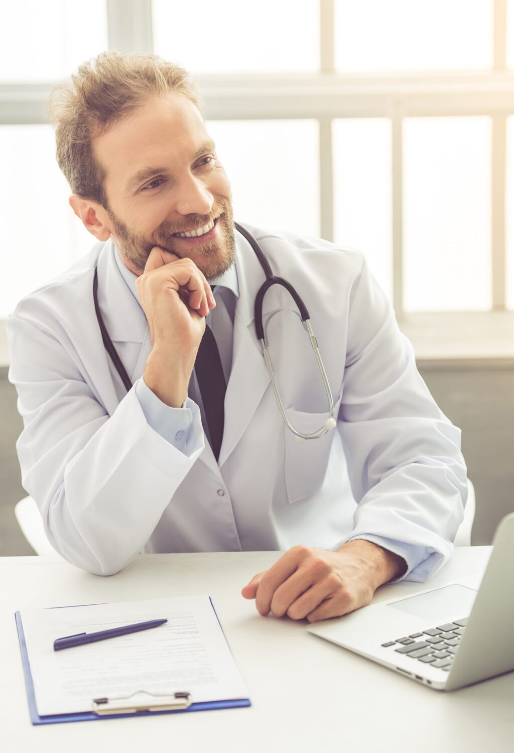 Handsome medical doctor Handsome medical doctor in white coat is looking away and smiling while sitting in his office